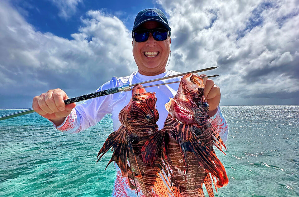Roger Muller, Jr. in Aruba holding two lionfish on a spear.
